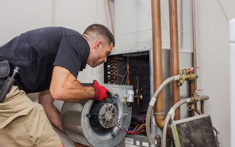 Professional HVAC technician in red gloves inspecting furnace blower motor and electrical connections during heating system maintenance.
