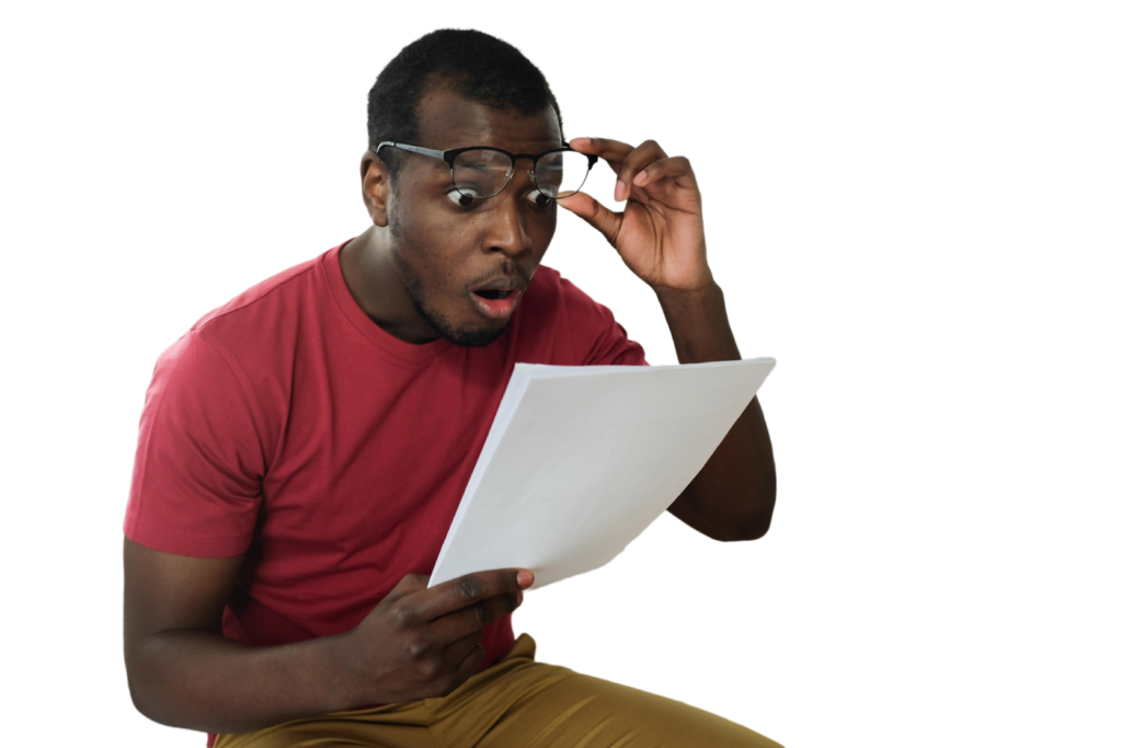 Man in red shirt and khaki pants wearing glasses holds a document with an astonished expression while adjusting his eyeglasses.