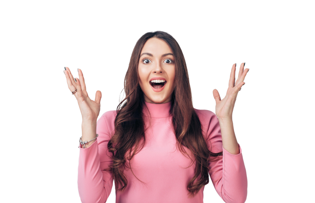 Woman with long brown hair wearing a pink turtleneck raises both hands with an excited, joyful expression against a white background.